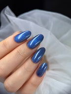 Hand with blue glittery nail polish against a white fabric background
