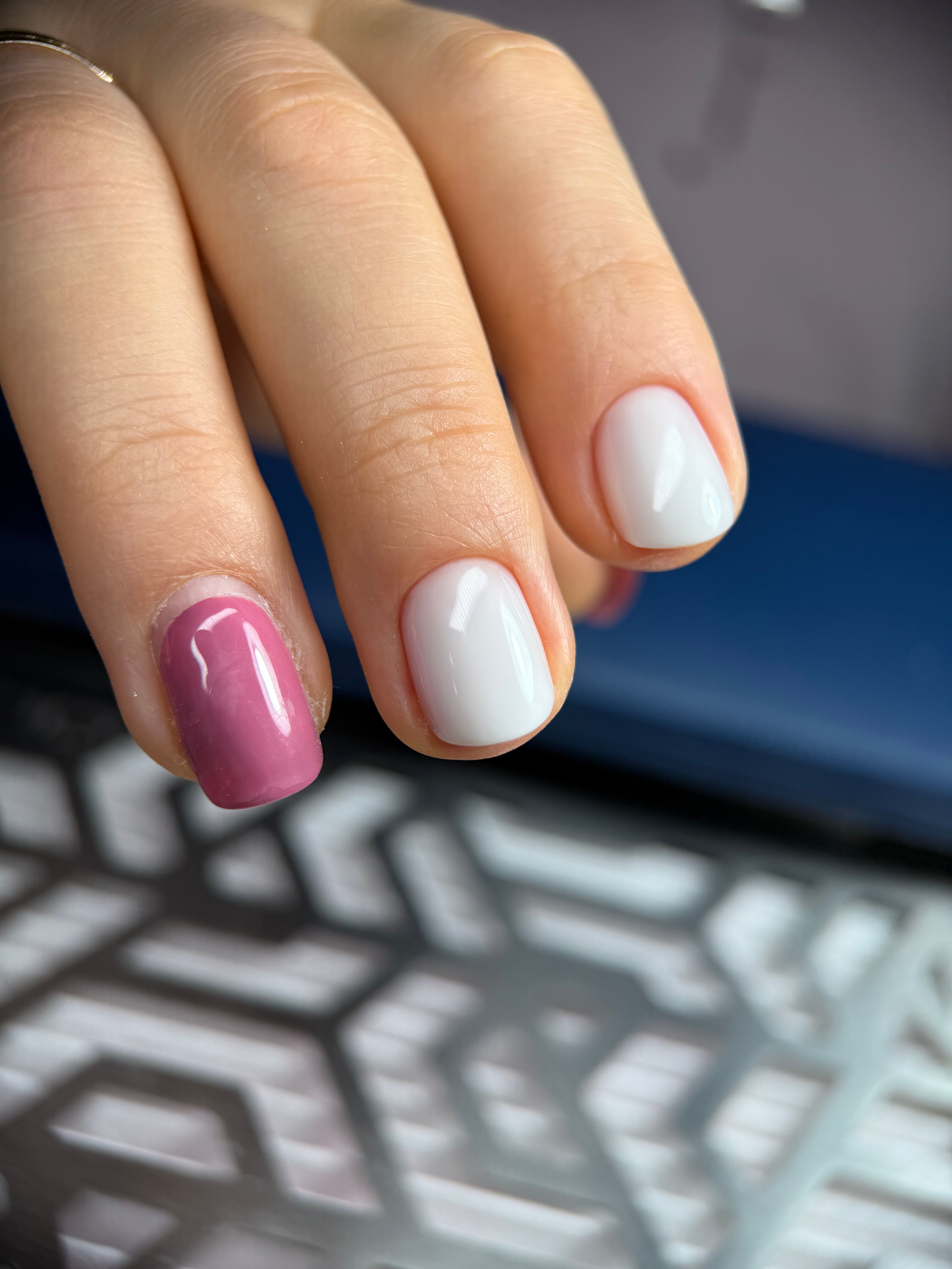 Close-up of a hand with white and pink nail polish against a blurred background