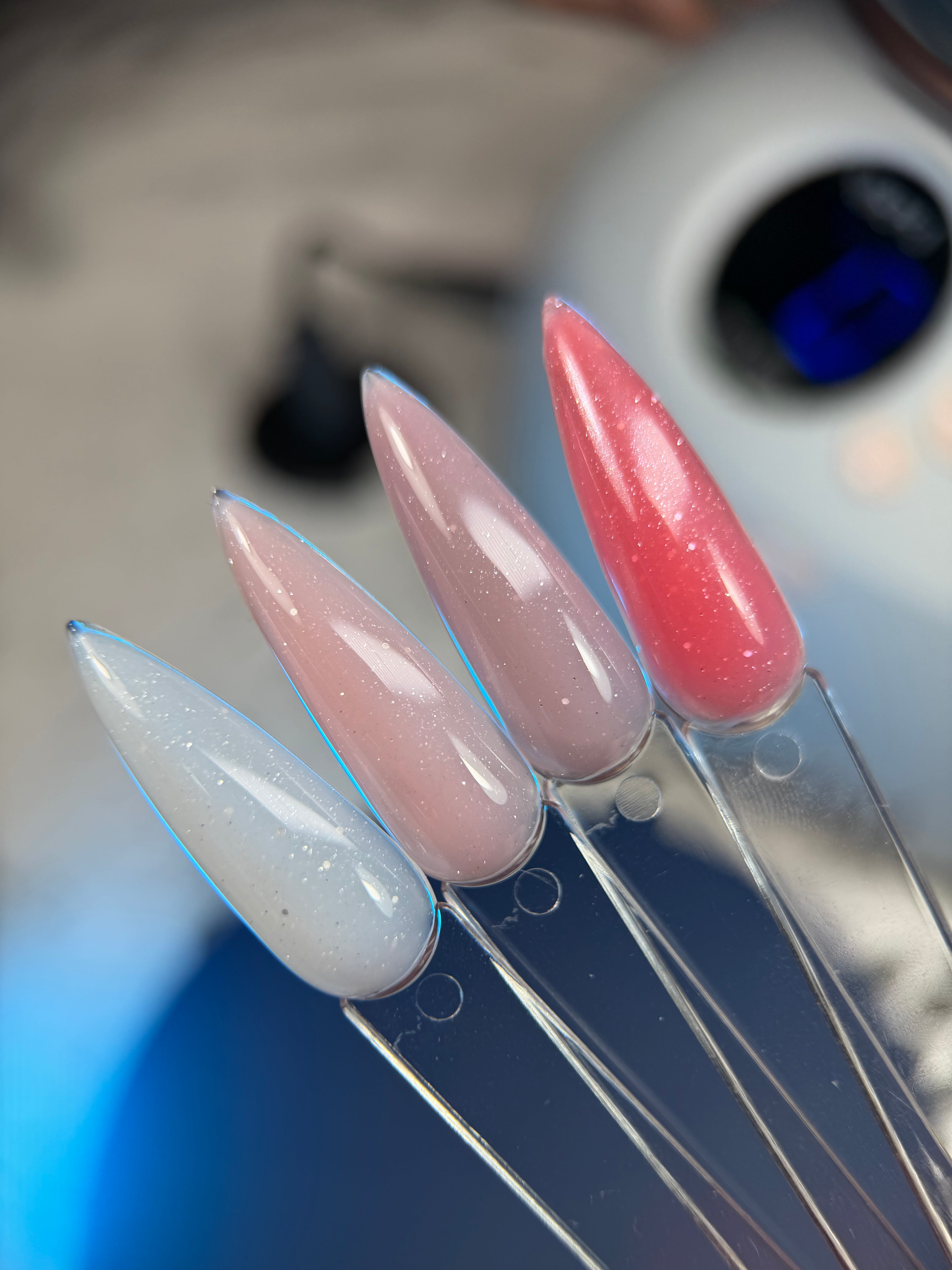 Set of long, pointed artificial nails in pink and white on a clear stand.