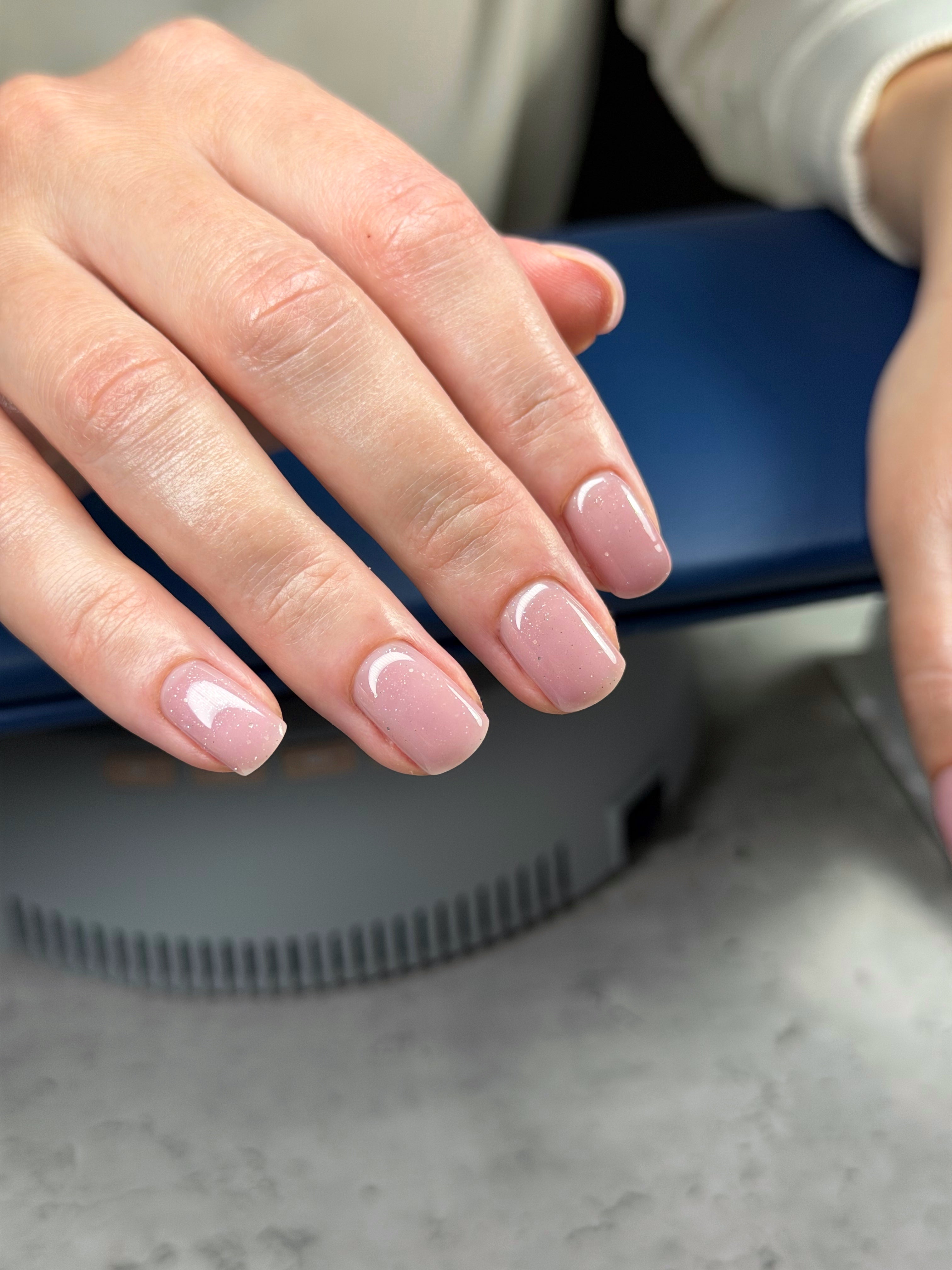 Close-up of hands with pink nail polish on a neutral background