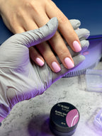 Hand with pink nail polish wearing a purple glove, with a bottle of nail polish in the background.