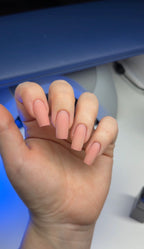 Hand with light pink nail polish against a blurred background