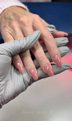 Close-up of a hand with painted nails being examined by a gloved hand. Builder gel