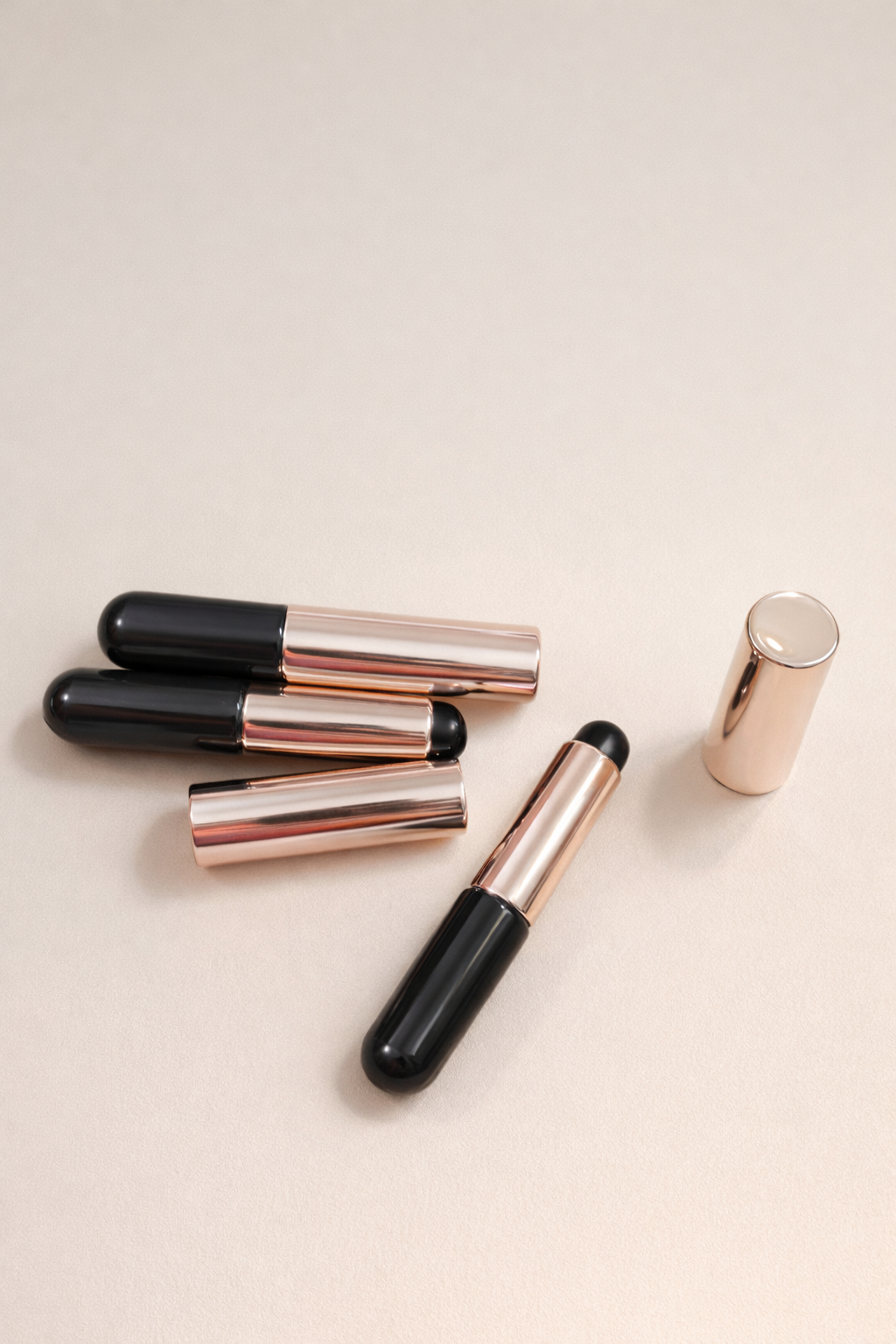 Set of lip glosses with black and rose gold accents on a light beige background