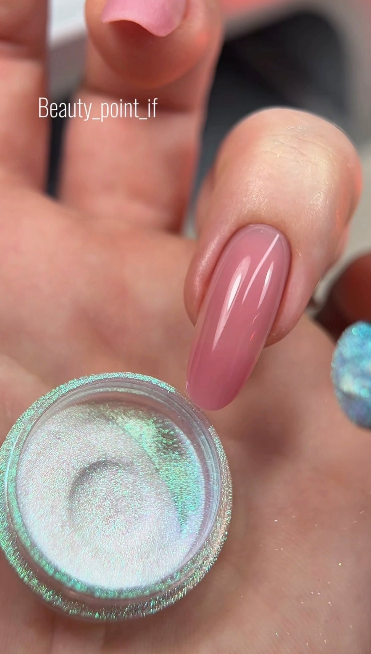 Hand holding a container of glitter with pink nails