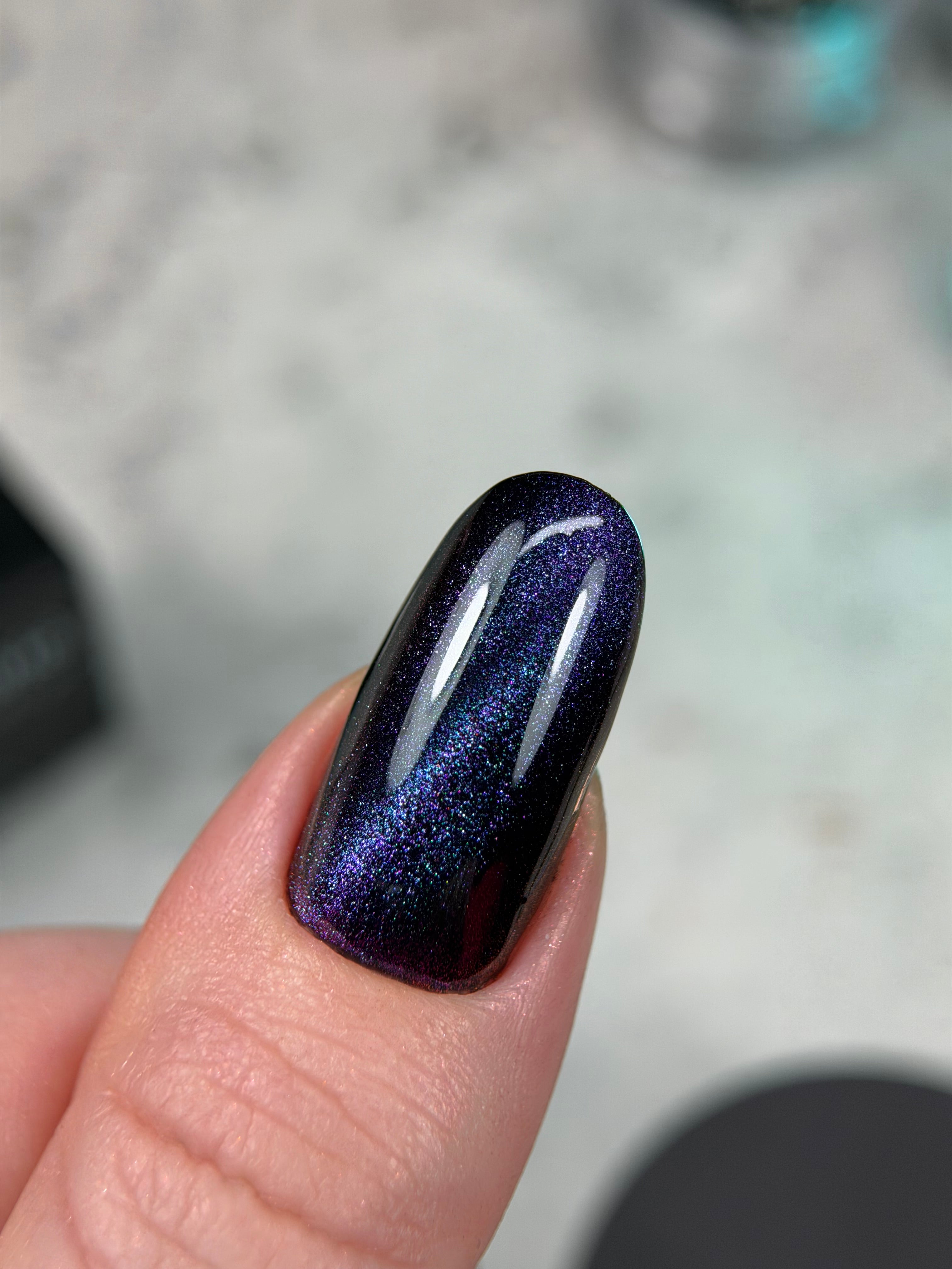 Nail with dark blue and purple glittery polish on a blurred background