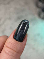 Black glittery nail polish on a finger with a blurred background