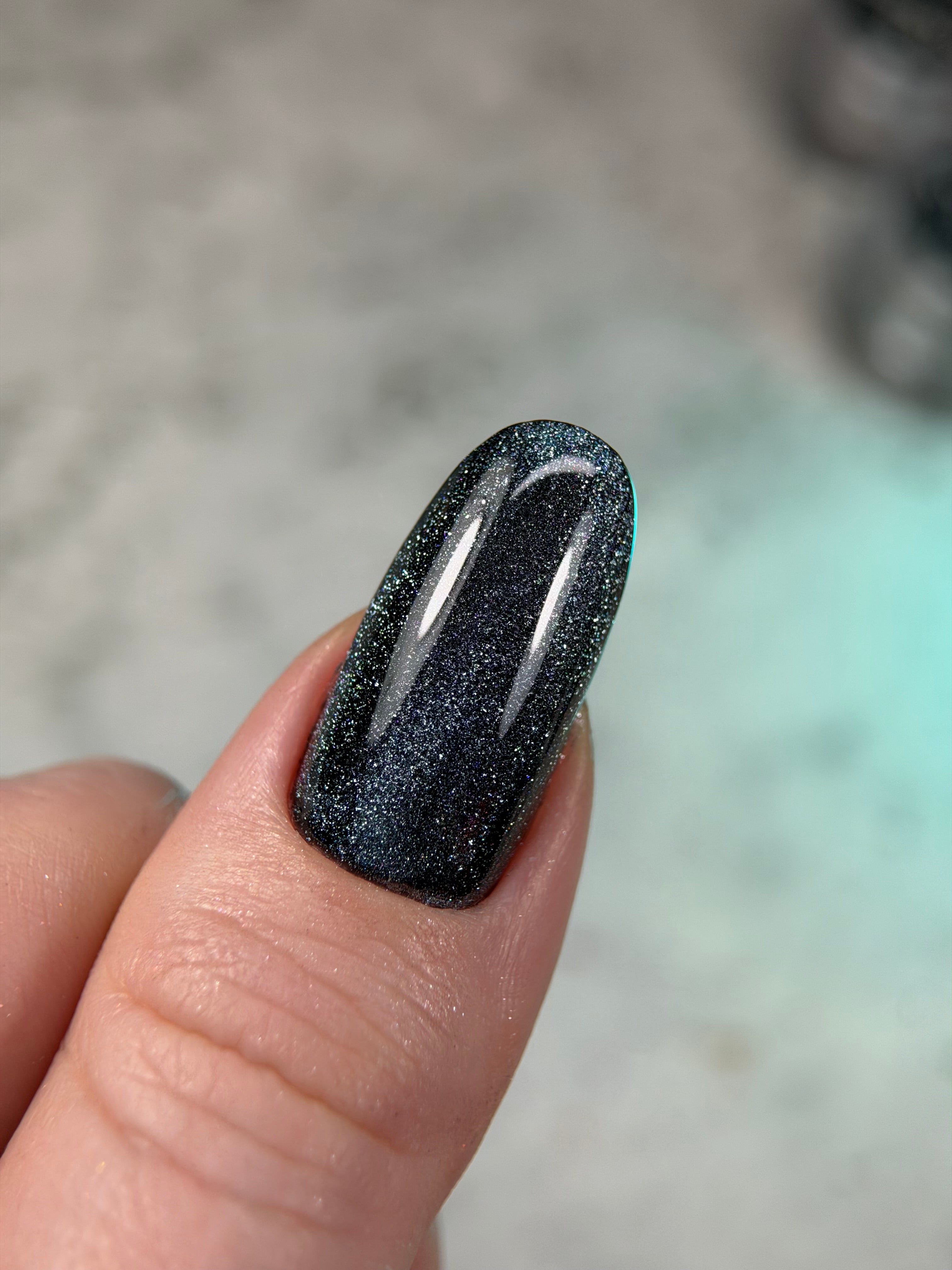 Black glittery nail polish on a finger with a blurred background