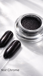 Black chrome nail polish in a jar with two nails painted with the same color on a reflective surface.