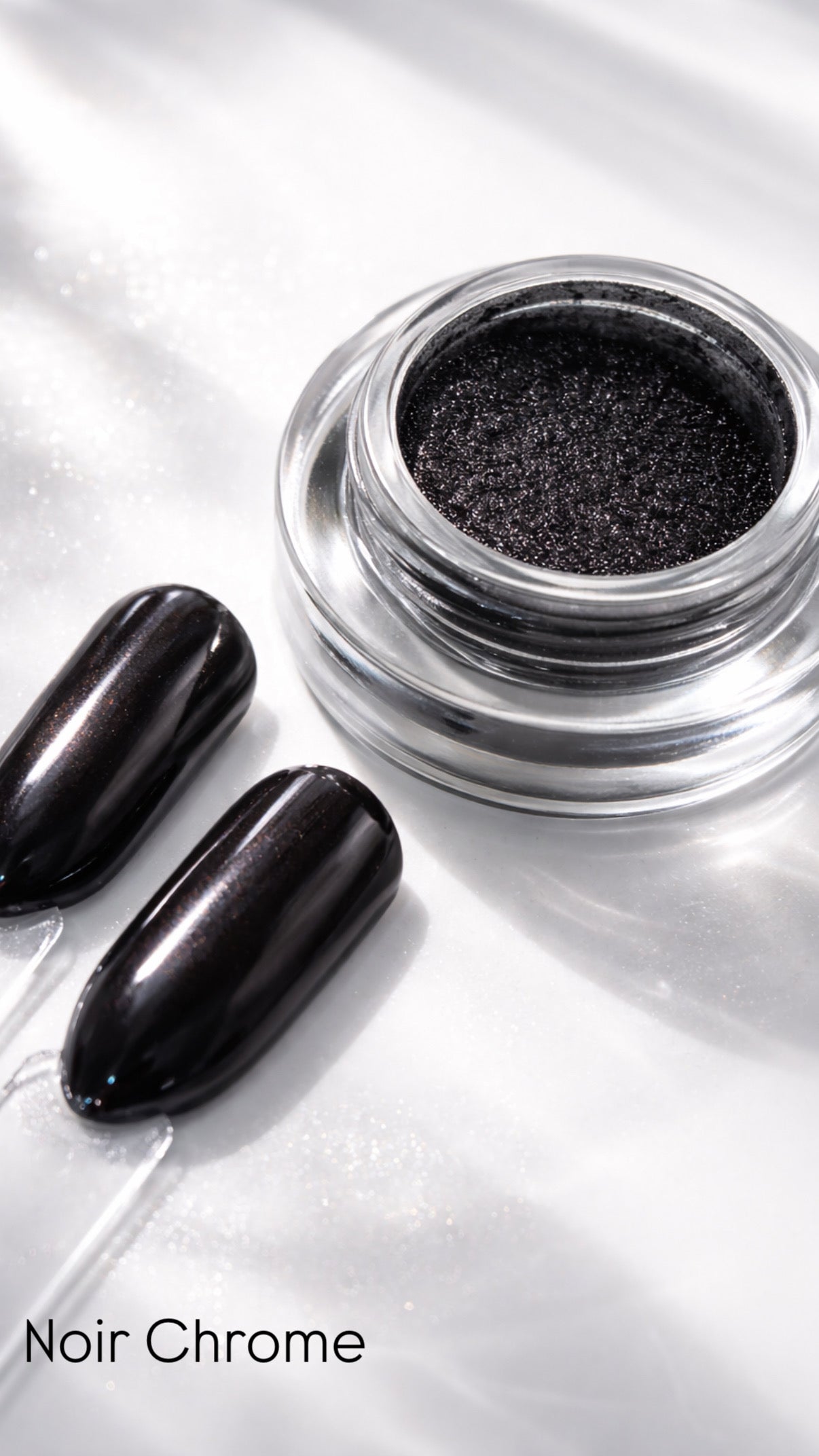 Black chrome nail polish in a jar with two nails painted with the same color on a reflective surface.