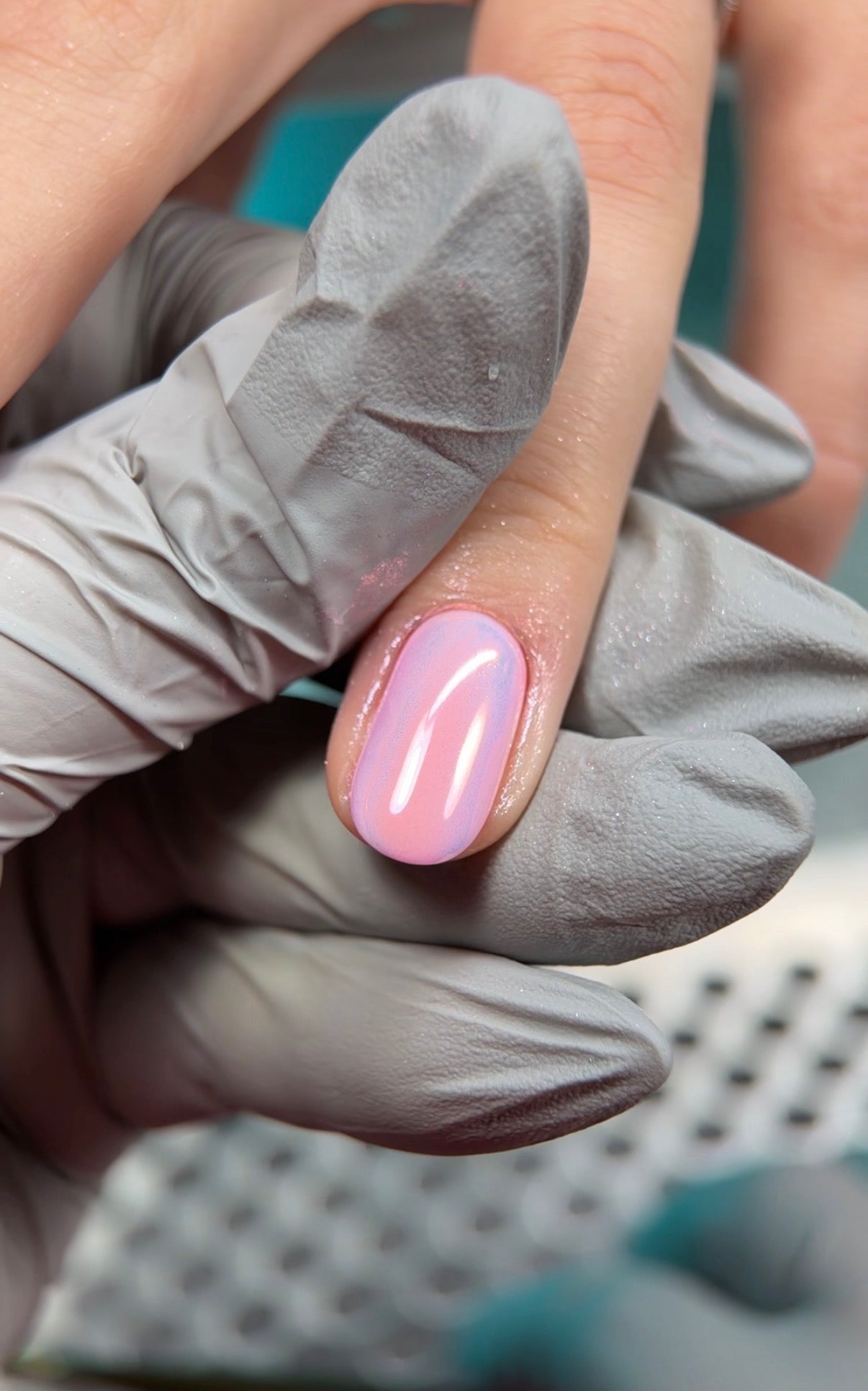 Hand with pink nail polish wearing a gray glove on a blurred background