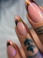 Close-up of a hand with pink nail polish and gold accents on a blurred background
