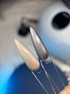 Close-up of a nail with a metallic tip and beige base, held by a tool against a blurred background.