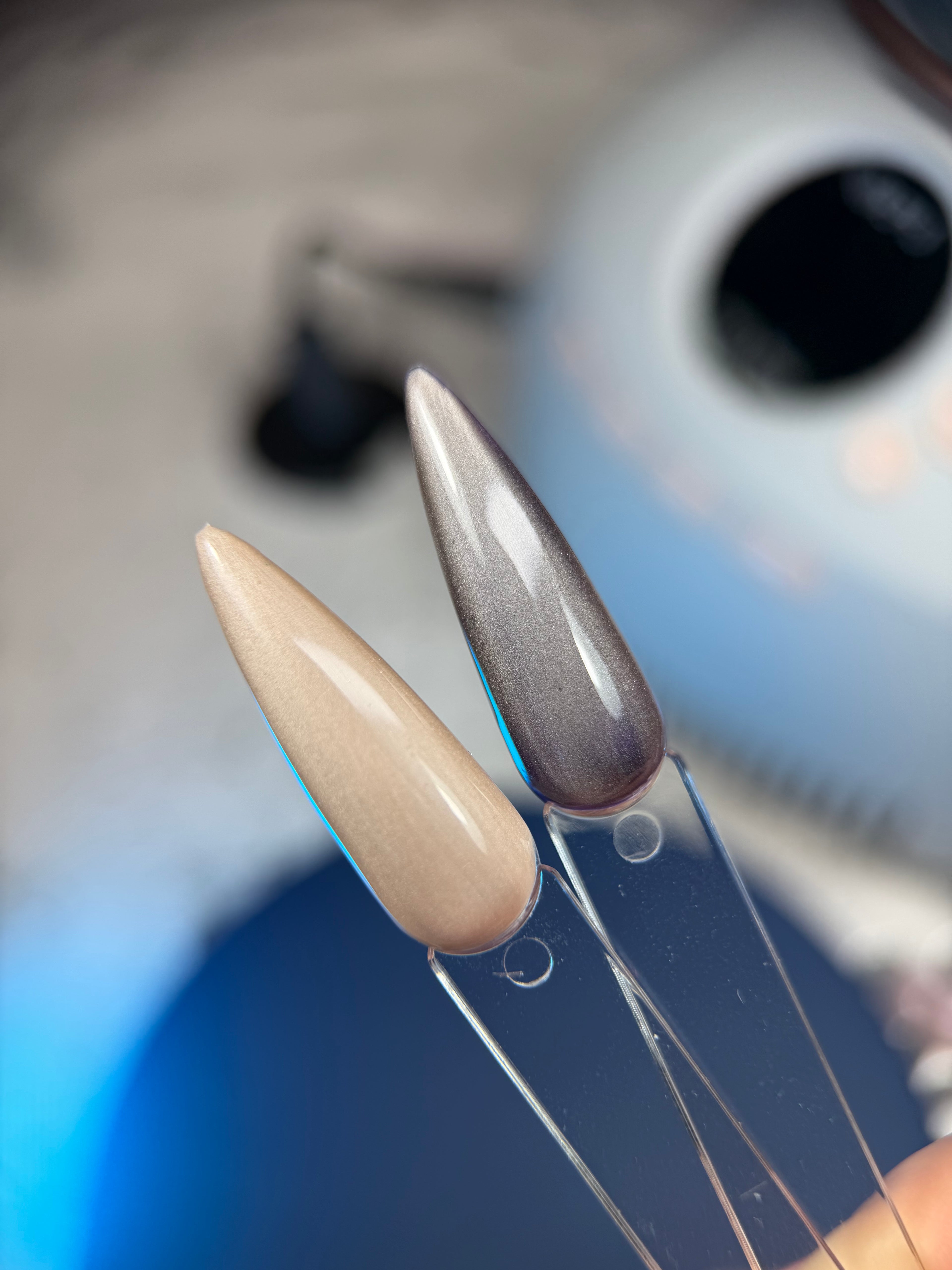 Close-up of a nail with a metallic tip and beige base, held by a tool against a blurred background.