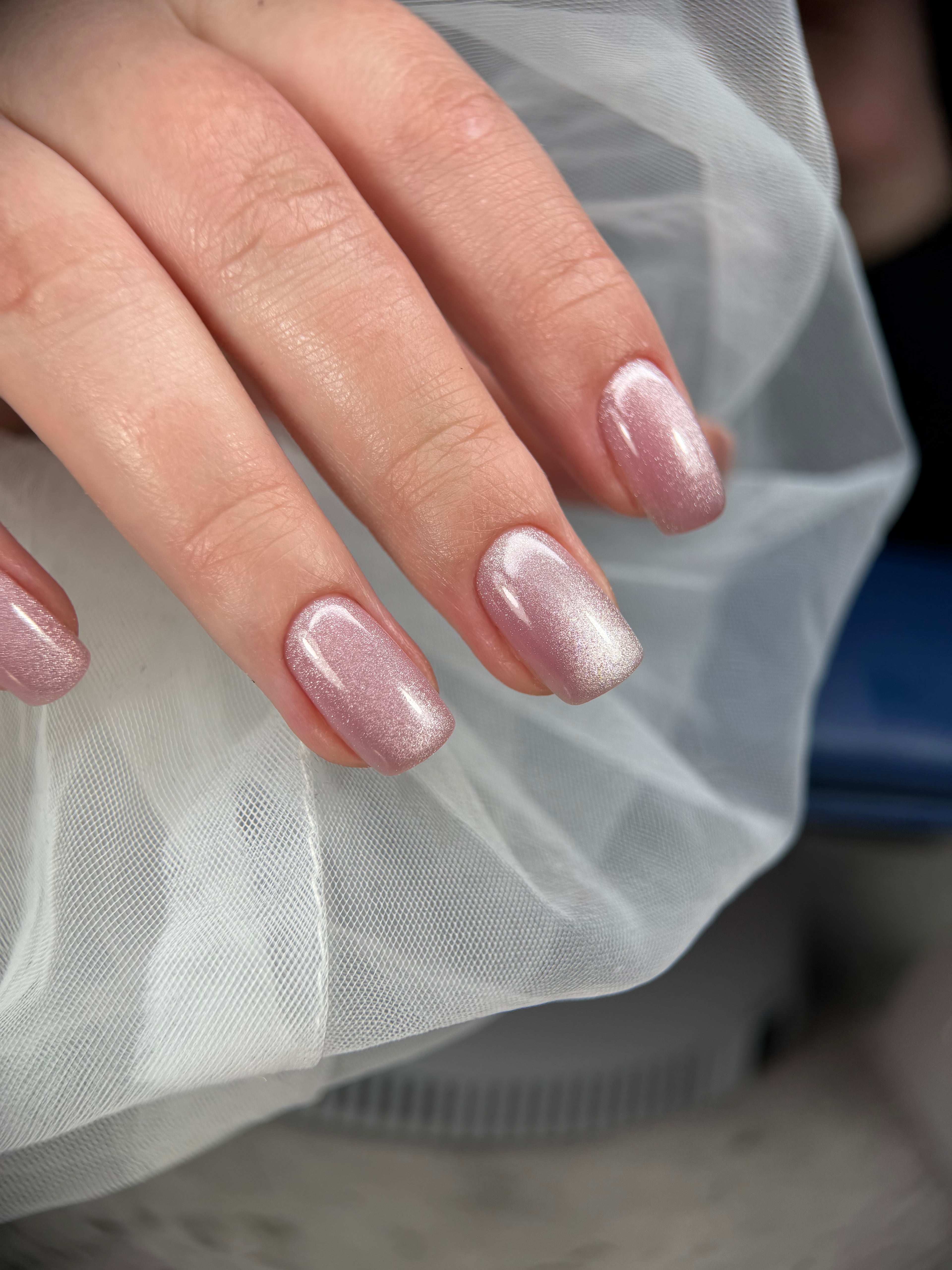 Hand with pink glittery nail polish against a white sheer fabric background