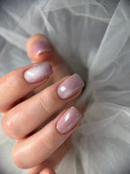 Close-up of a hand with pink glittery nail polish against a soft white background