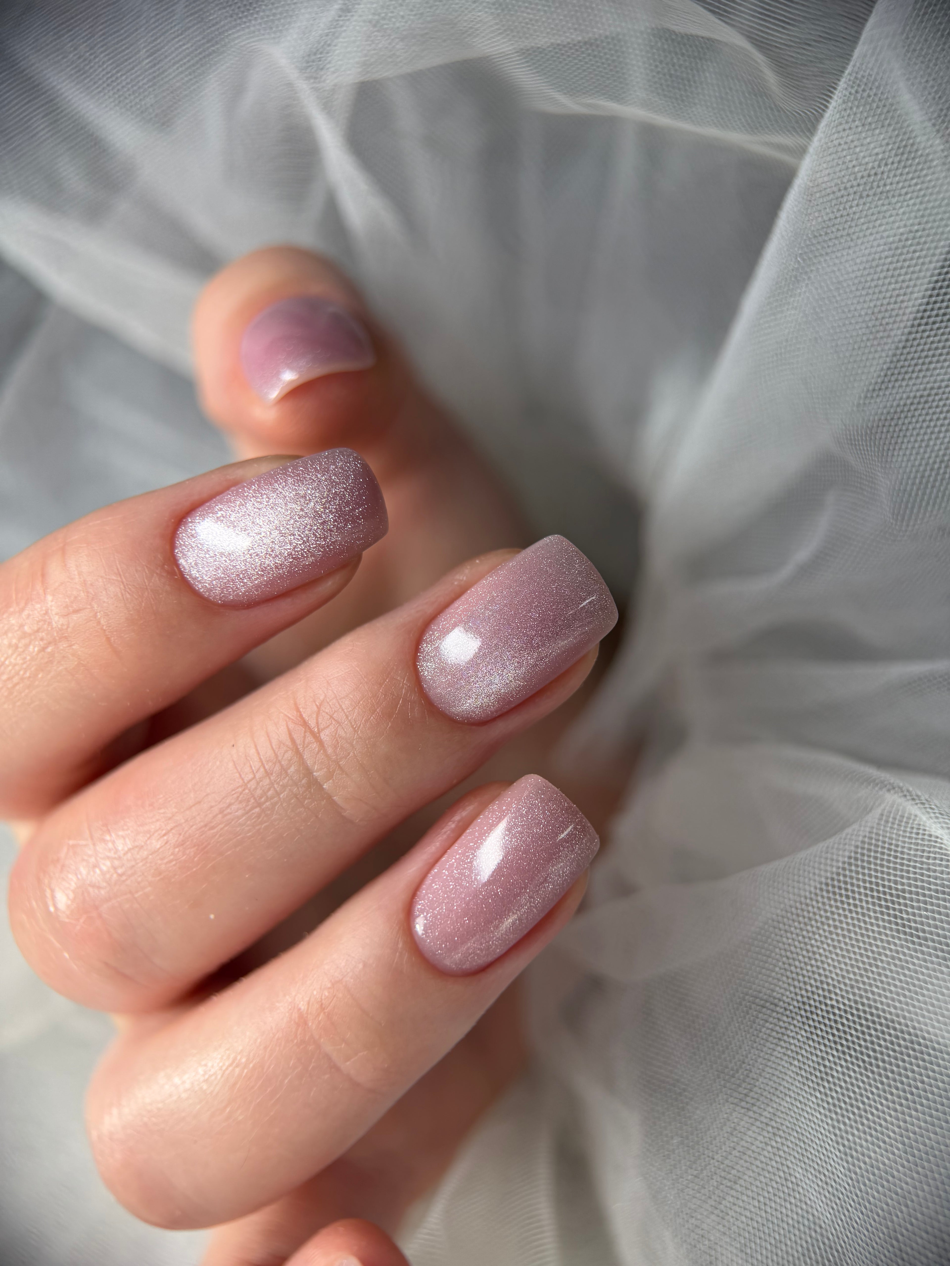Close-up of a hand with pink glittery nail polish against a soft white background