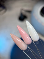 Close-up of long, pointed nails in white, pink, and beige on a blurred background.